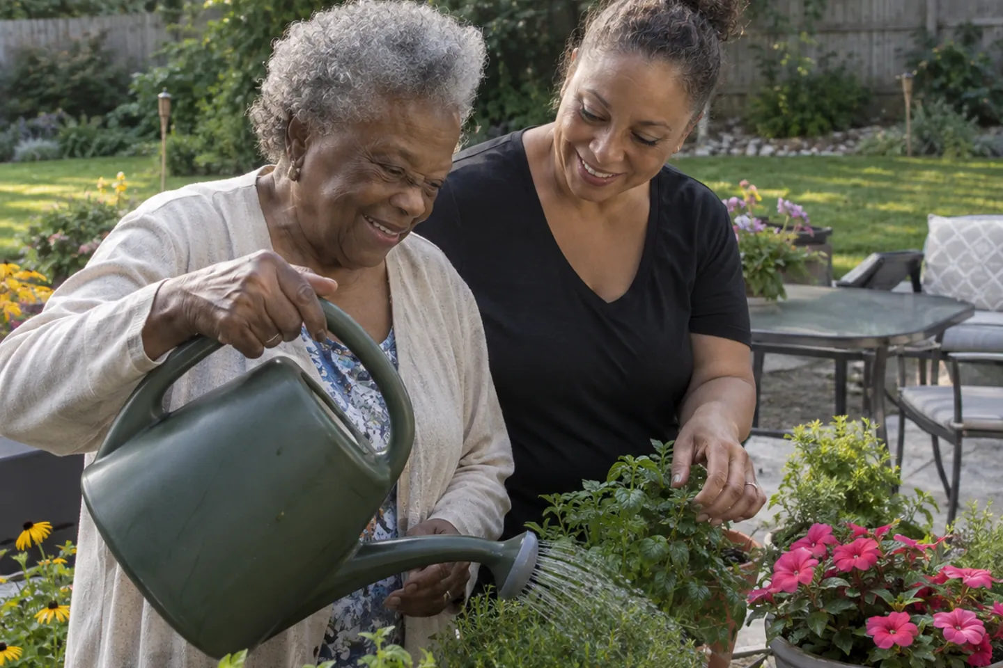 A resident watering flowers with a caregiver